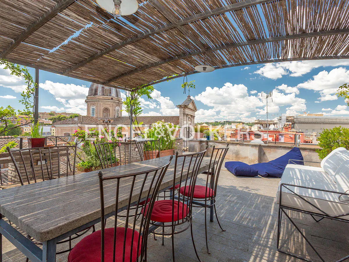 Rooftop terrace with a stone dining table, red-cushioned chairs, a white sofa, and a view of historic city domes.