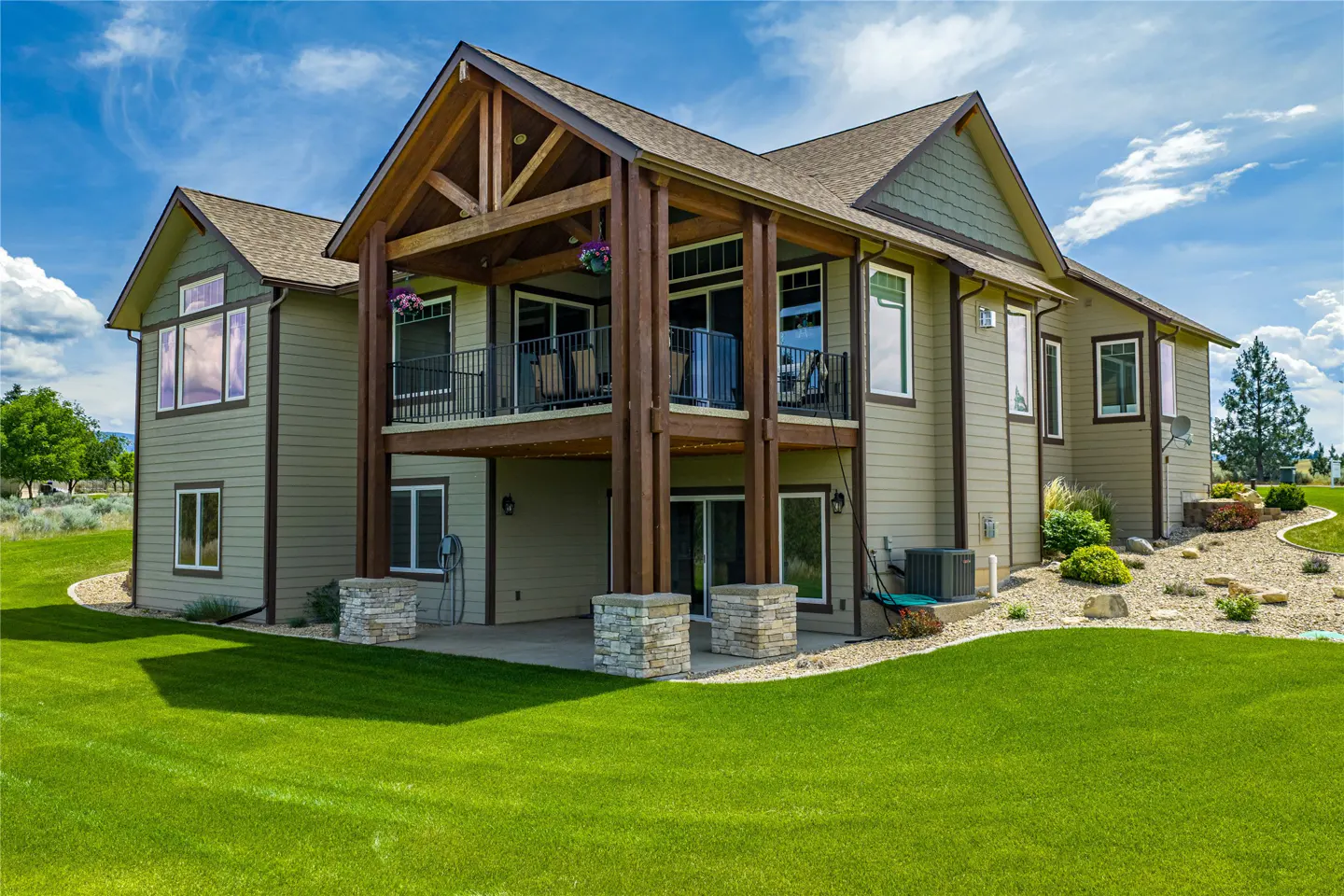 Two-story house with a brown roof, green siding, and a large wooden balcony overlooking a green lawn.
