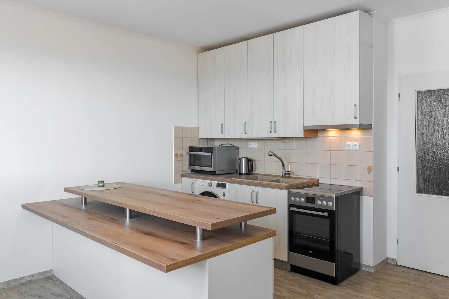 Bright kitchen with white cabinets, stainless steel appliances, and a wood countertop island. A washing machine is visible under the counter.