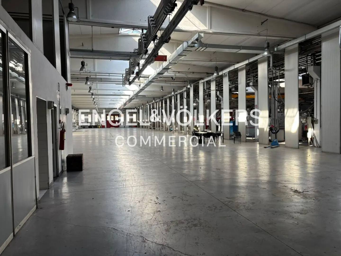 A large, empty commercial space with white walls, gray floors, and overhead lighting.
