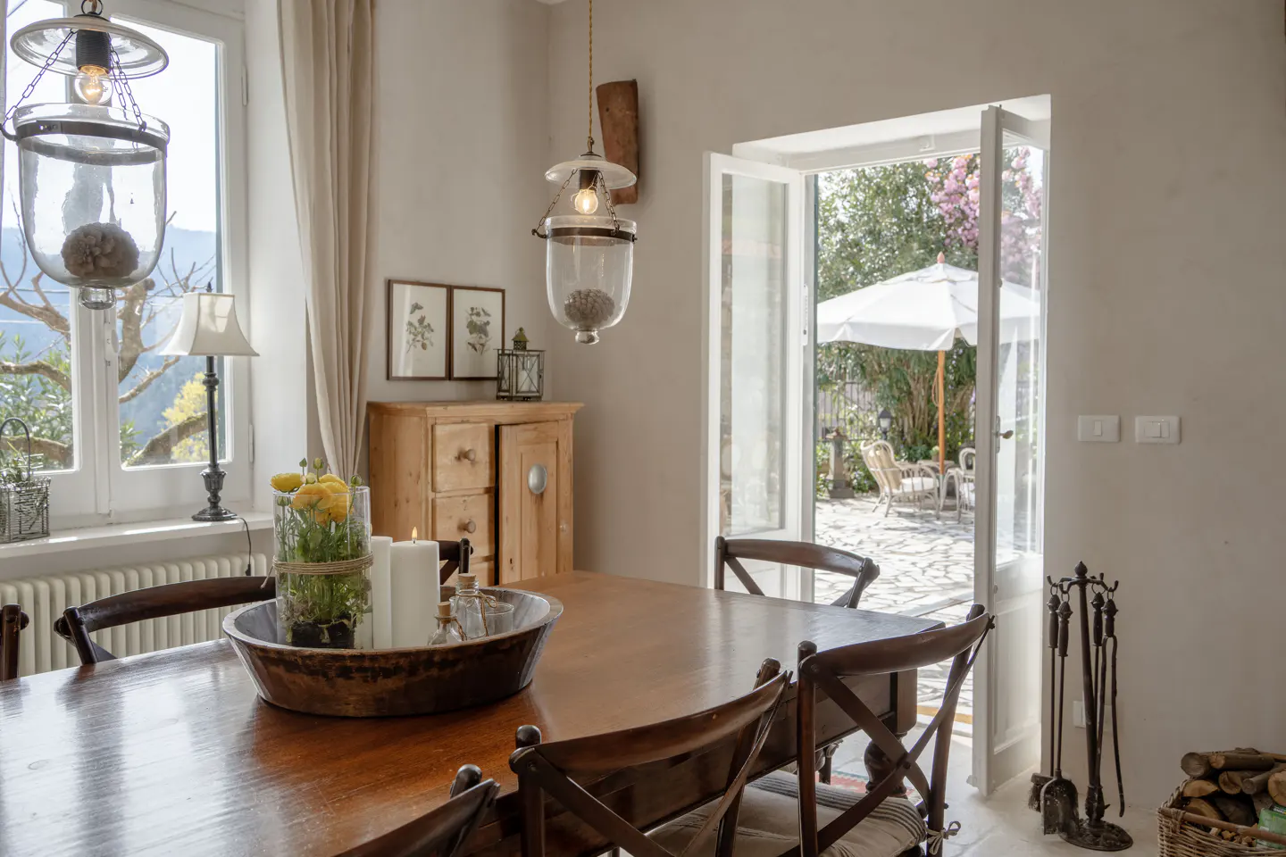 A dining room with a wooden table, chairs, and an open door to a patio with a white umbrella.