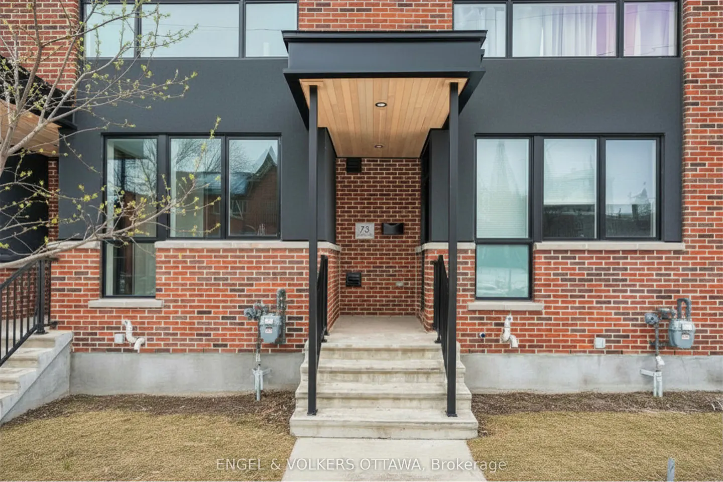 Brick townhouse with black trim and large windows. Concrete steps lead to a covered porch with a light wood ceiling. Address number 73 is visible.