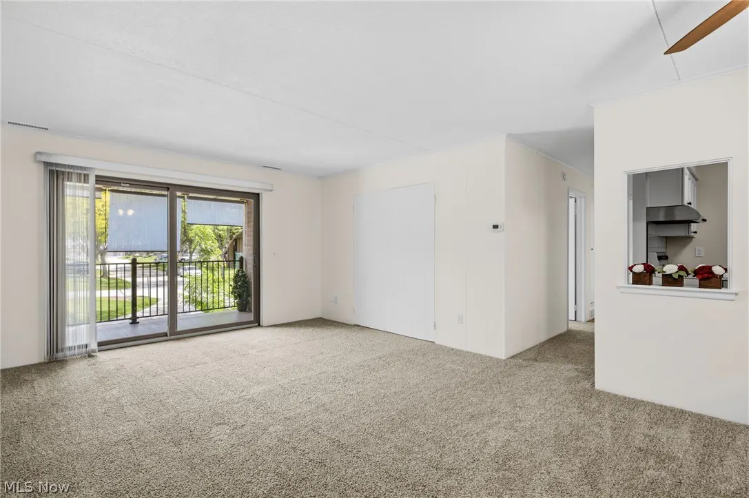 Bright living room with beige carpet, white walls, and sliding glass doors to a balcony. A kitchen pass-through is visible.