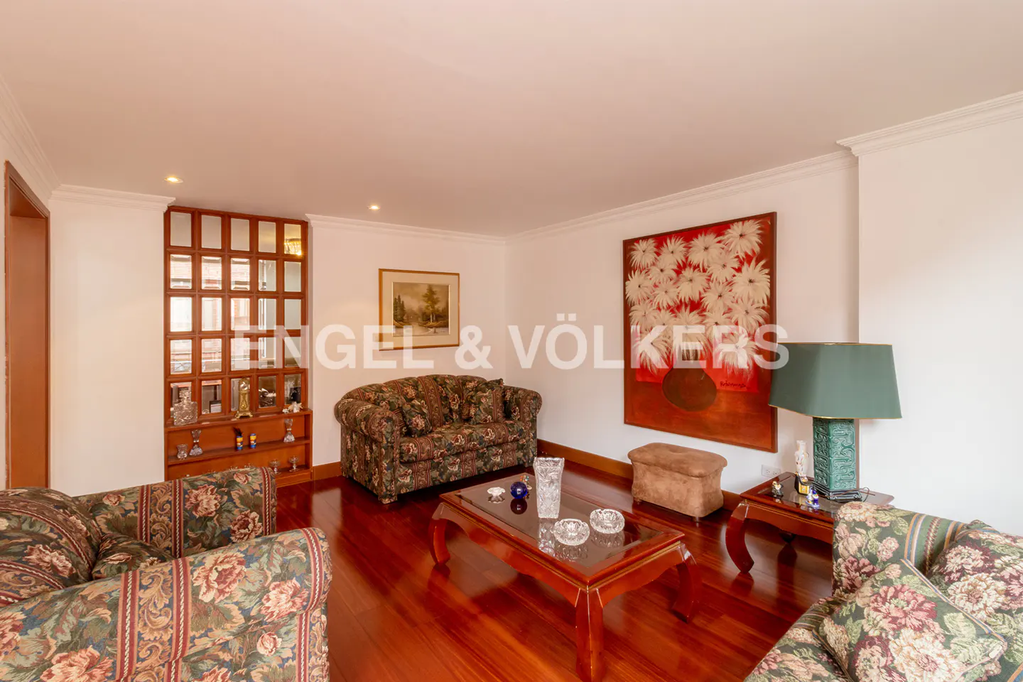 Living room with floral sofas, wood floors, coffee table, and a large painting of white flowers.