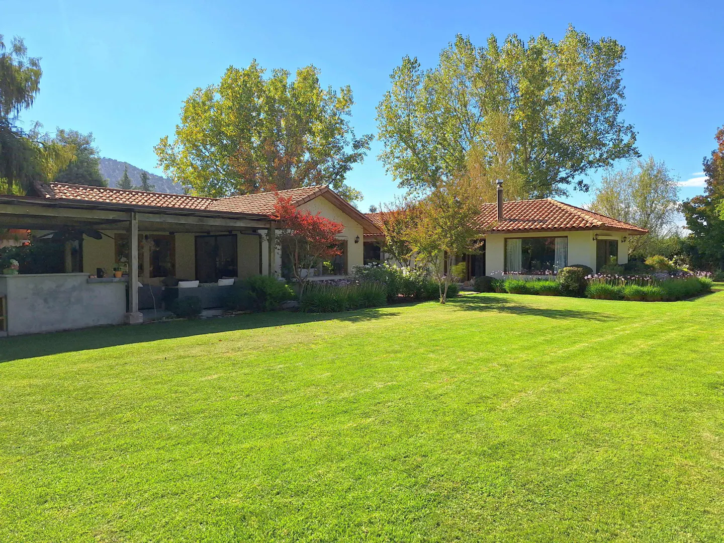 A single-story house with a red tile roof and a large green lawn on a sunny day.