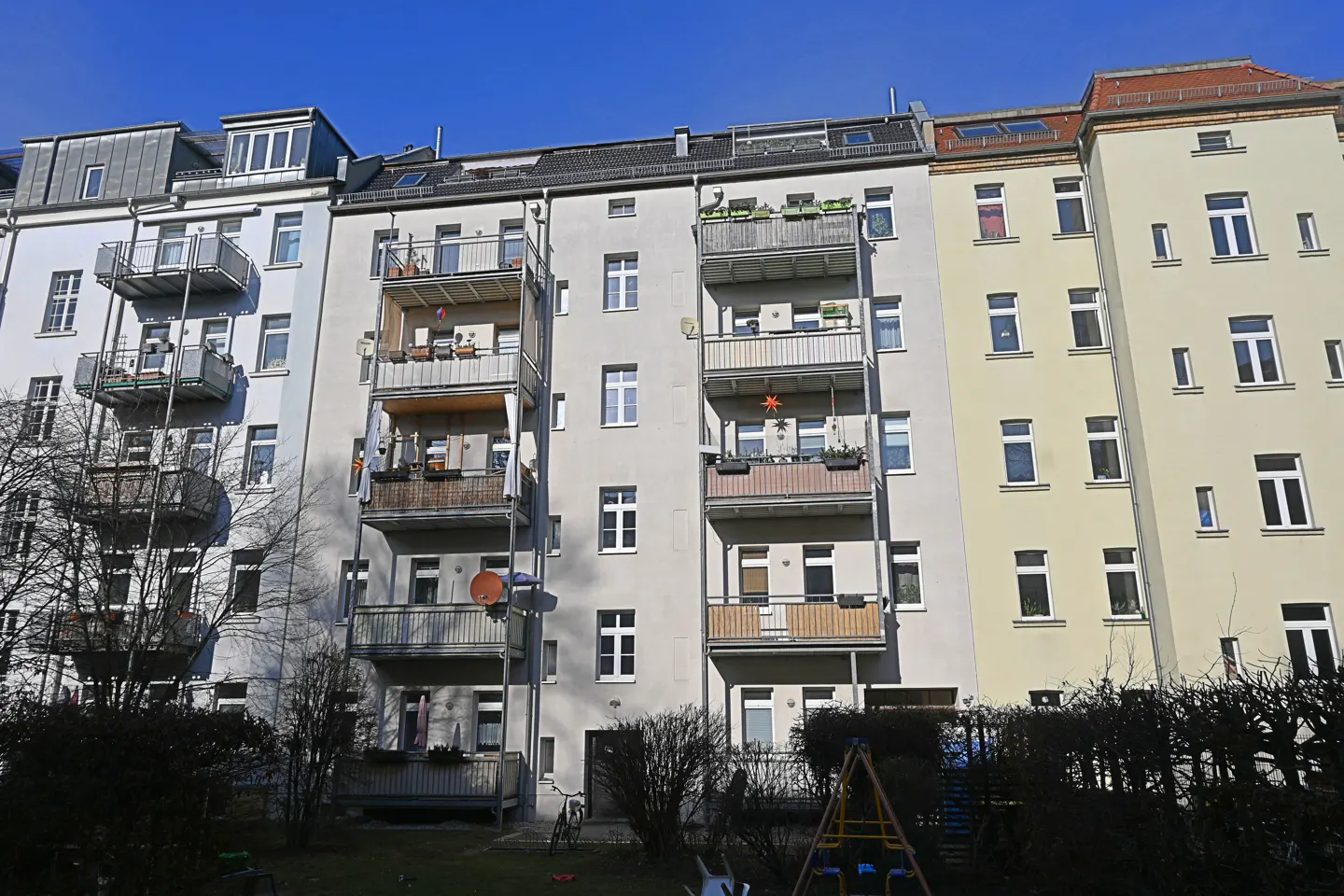 Exterior view of three apartment buildings with balconies under a blue sky.