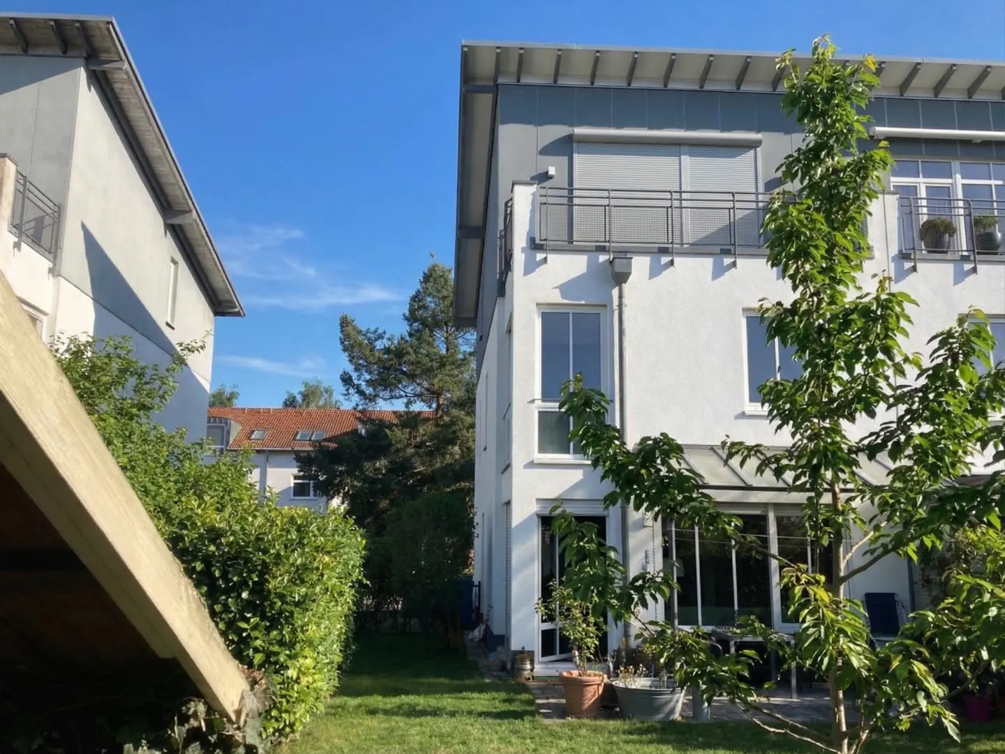 Exterior view of a modern white two-story house with a gray roof, a balcony, and a green lawn.