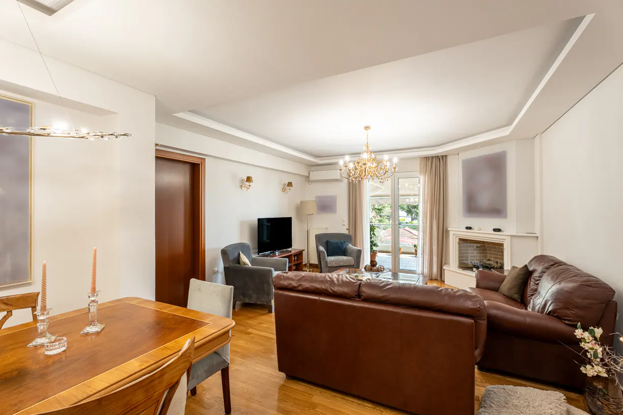 A bright living room with hardwood floors, brown leather sofas, gray armchairs, and a wooden dining table.