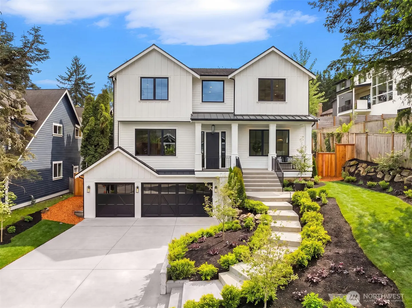 Two-story white farmhouse with black trim, a two-car garage, and landscaped front yard on a sunny day.