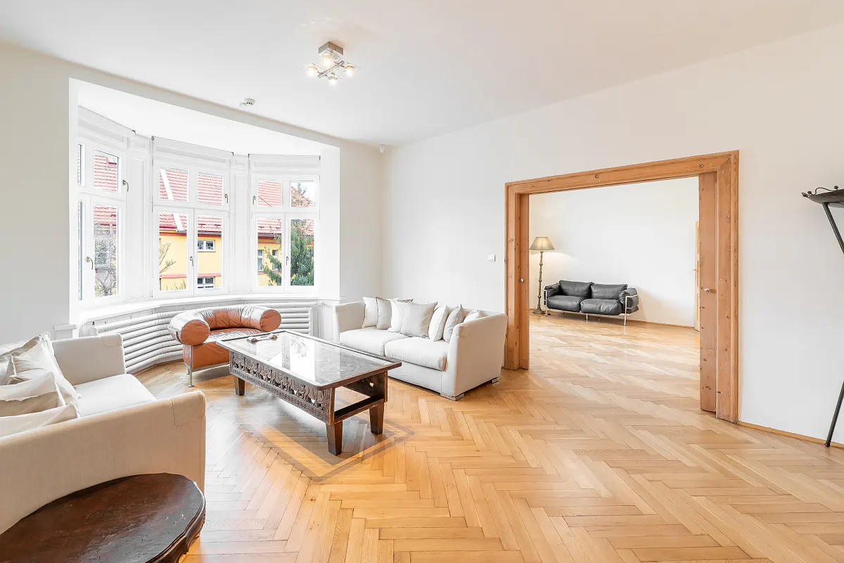 Bright living room with herringbone wood floors, white sofas, a coffee table, and a doorway to an adjacent room.