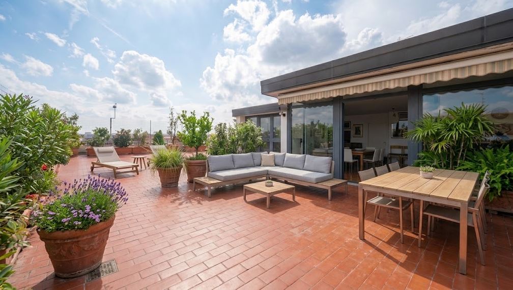 Spacious rooftop terrace with terracotta tiles, grey sectional sofa, wooden dining set, lounge chair, and potted plants. [AI-generated text] [AI-modified]