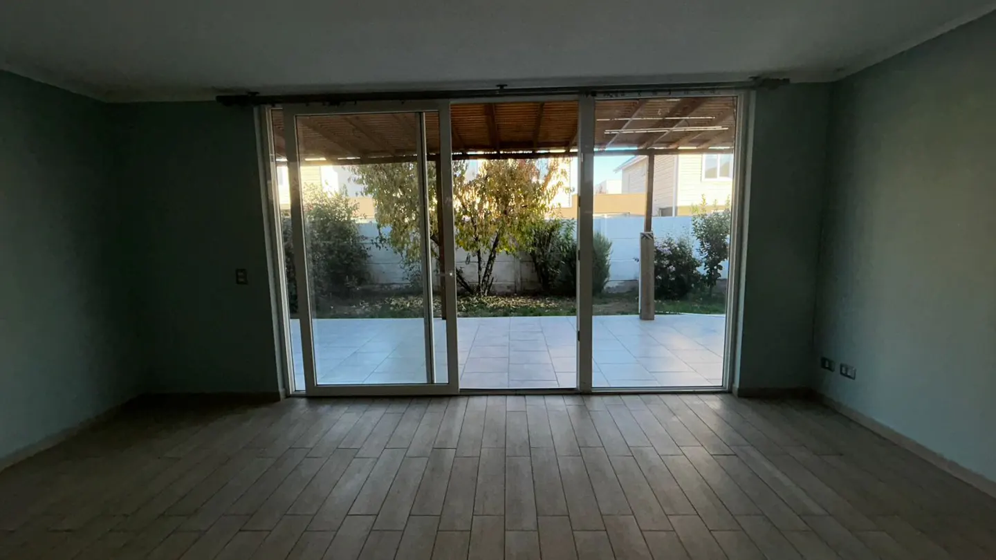 Empty room with light green walls and wood floors. Sliding glass doors open to a patio and garden.