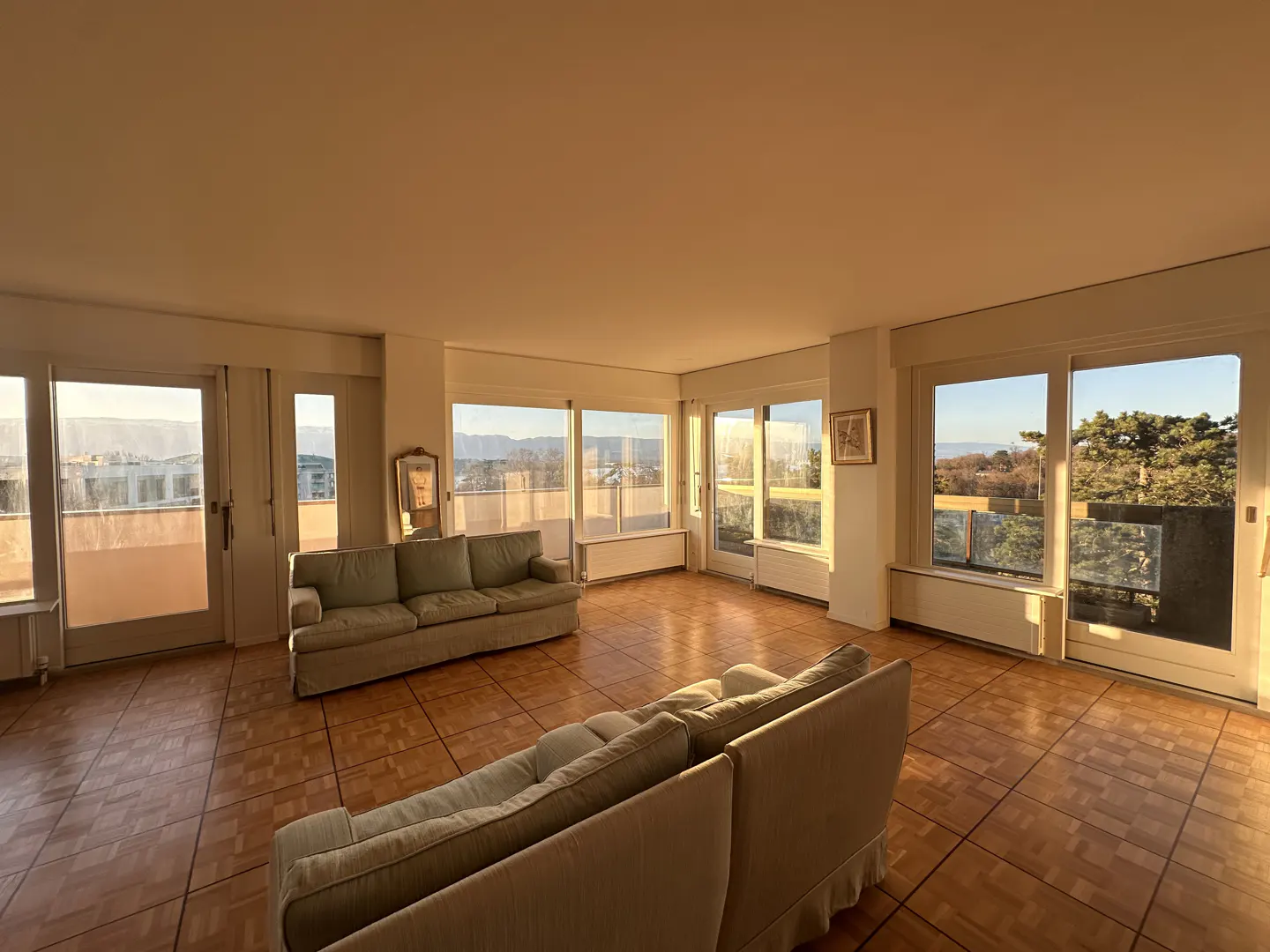 Spacious living room with parquet floors, two sofas, and large windows with city views.