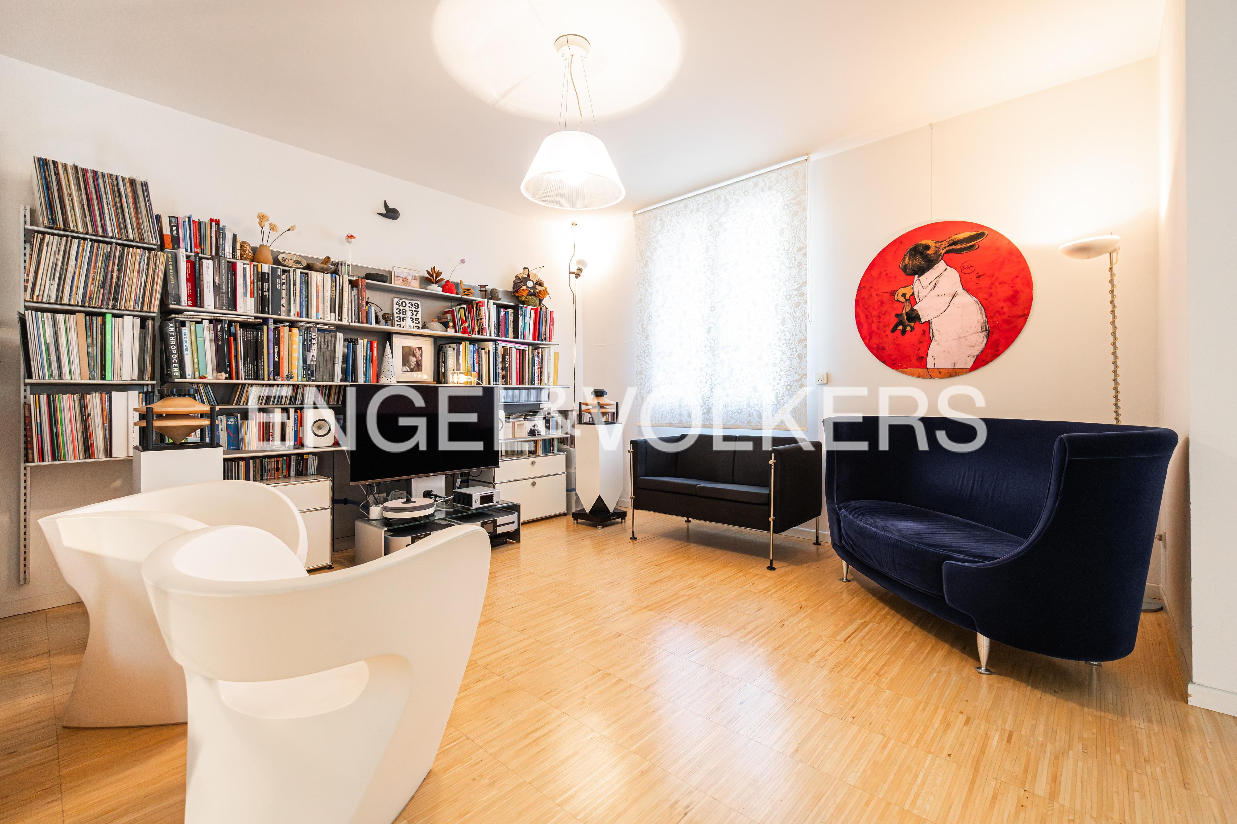 Bright living room with a large bookshelf, white chairs, black and blue sofas, and a red painting of a rabbit.