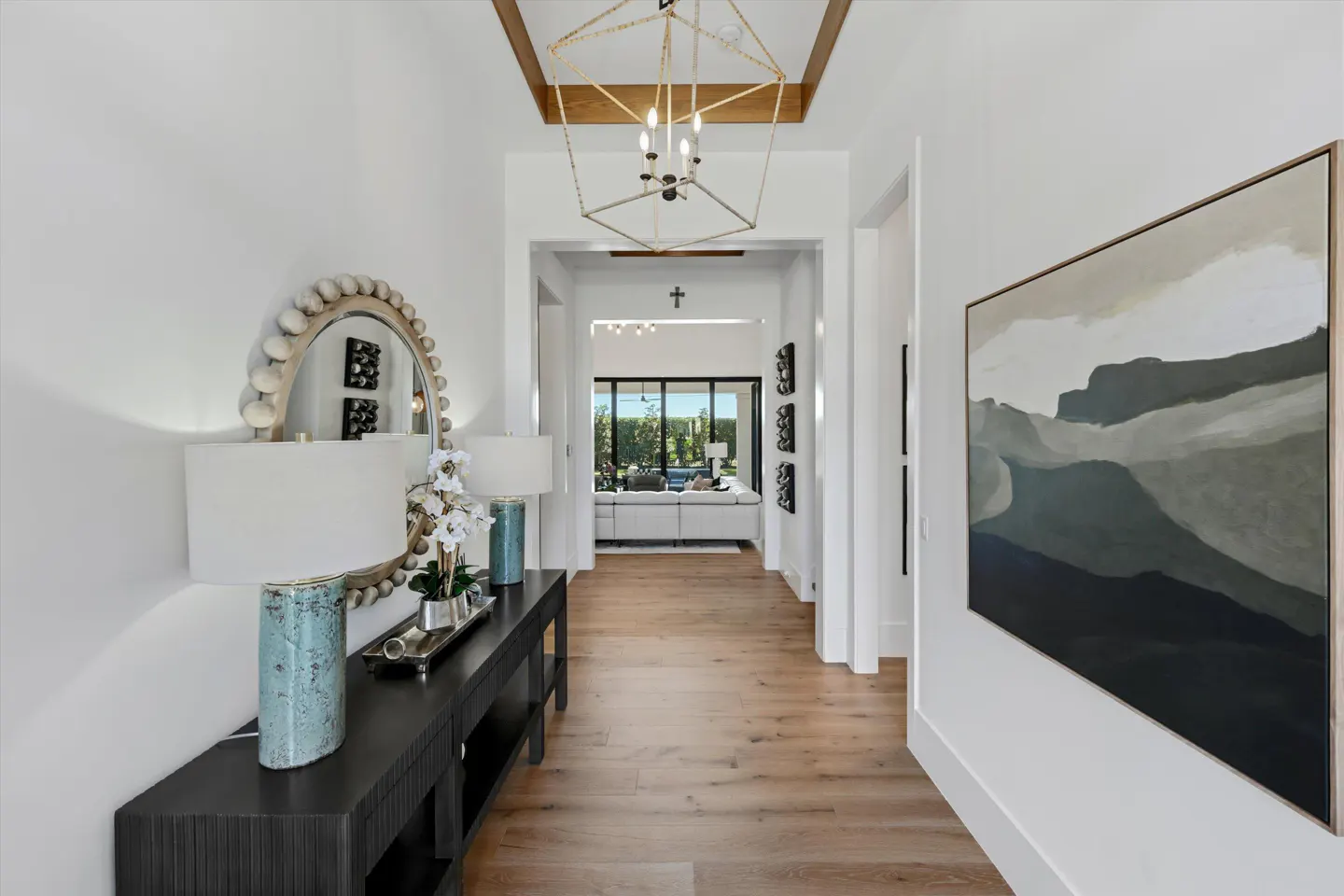 Entryway with wood floors, white walls, and a black console table with lamps and a mirror. A geometric chandelier hangs from the ceiling.