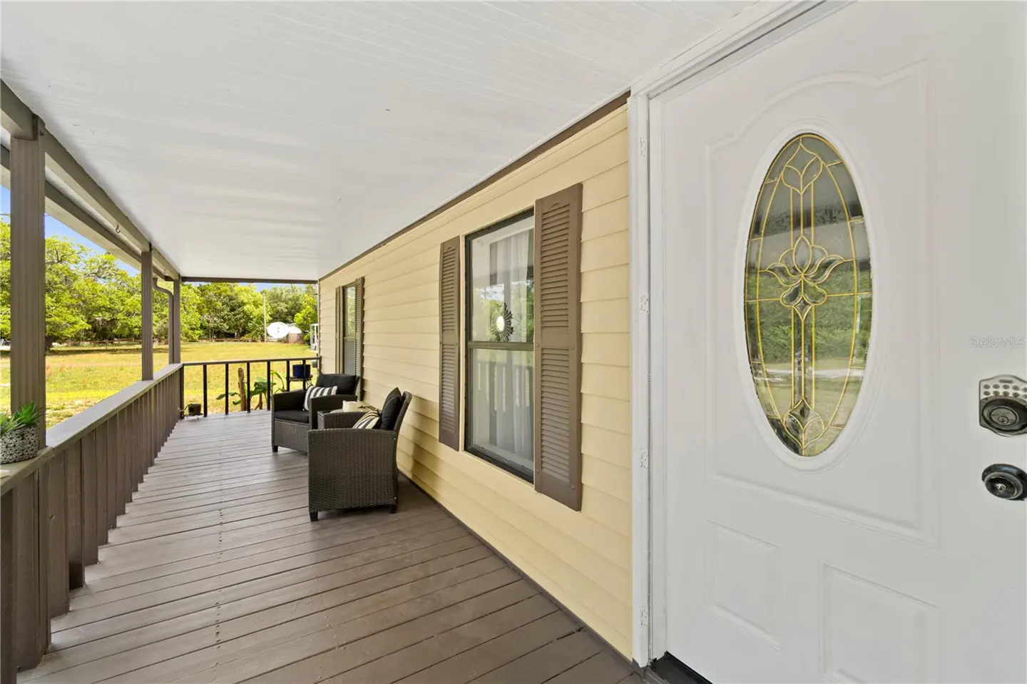 Covered porch with seating. The house is light yellow with brown shutters and a white front door with an oval window.