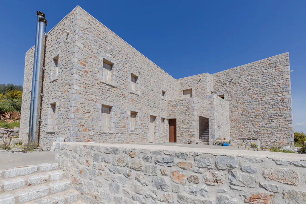 Exterior view of a two-story stone house with a metal chimney against a clear blue sky.