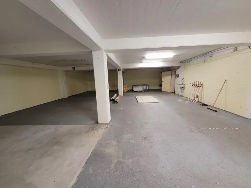 An empty, spacious basement with light yellow walls, a grey concrete floor, white support pillars, and overhead lighting.