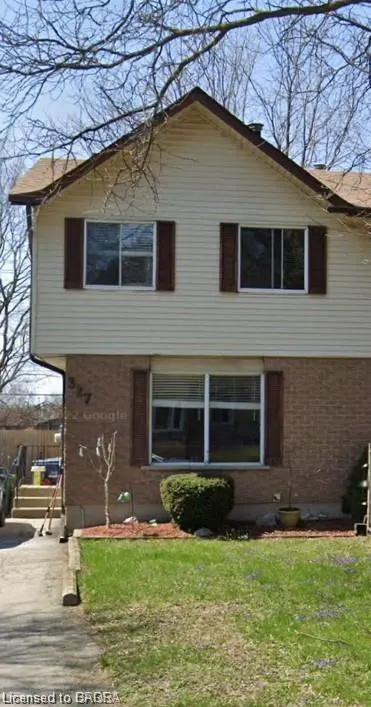 Two-story house with tan siding, brick facade, brown shutters, and a green lawn.