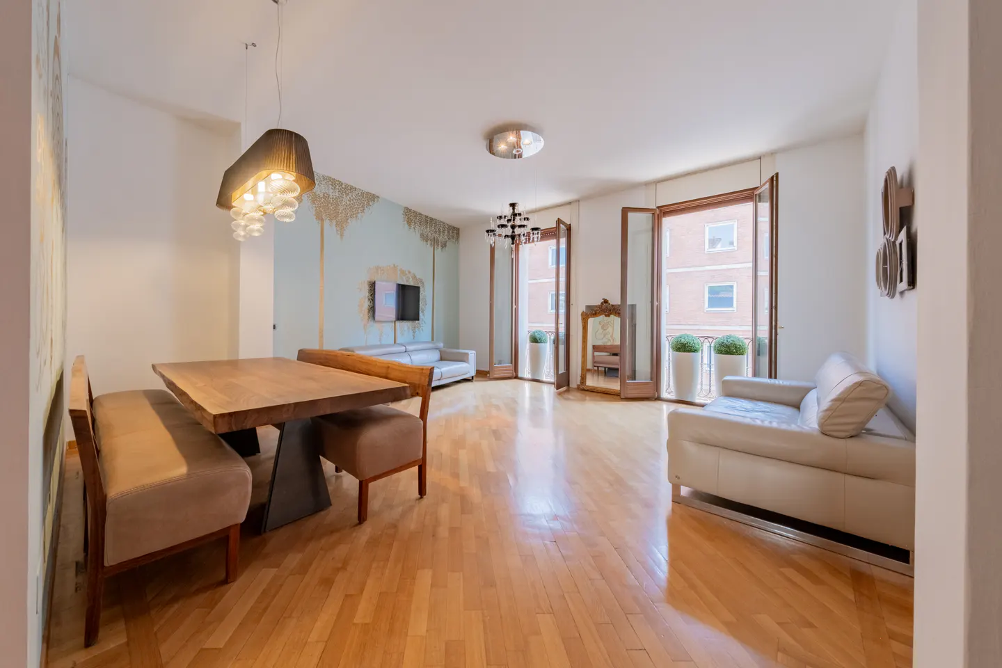 Bright apartment with hardwood floors, a dining table with bench seating, and a living area with a white sofa and balcony.