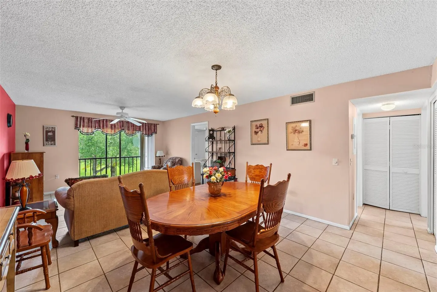 A living and dining area with a wooden table, chairs, and a tan sofa. A chandelier hangs above the table.