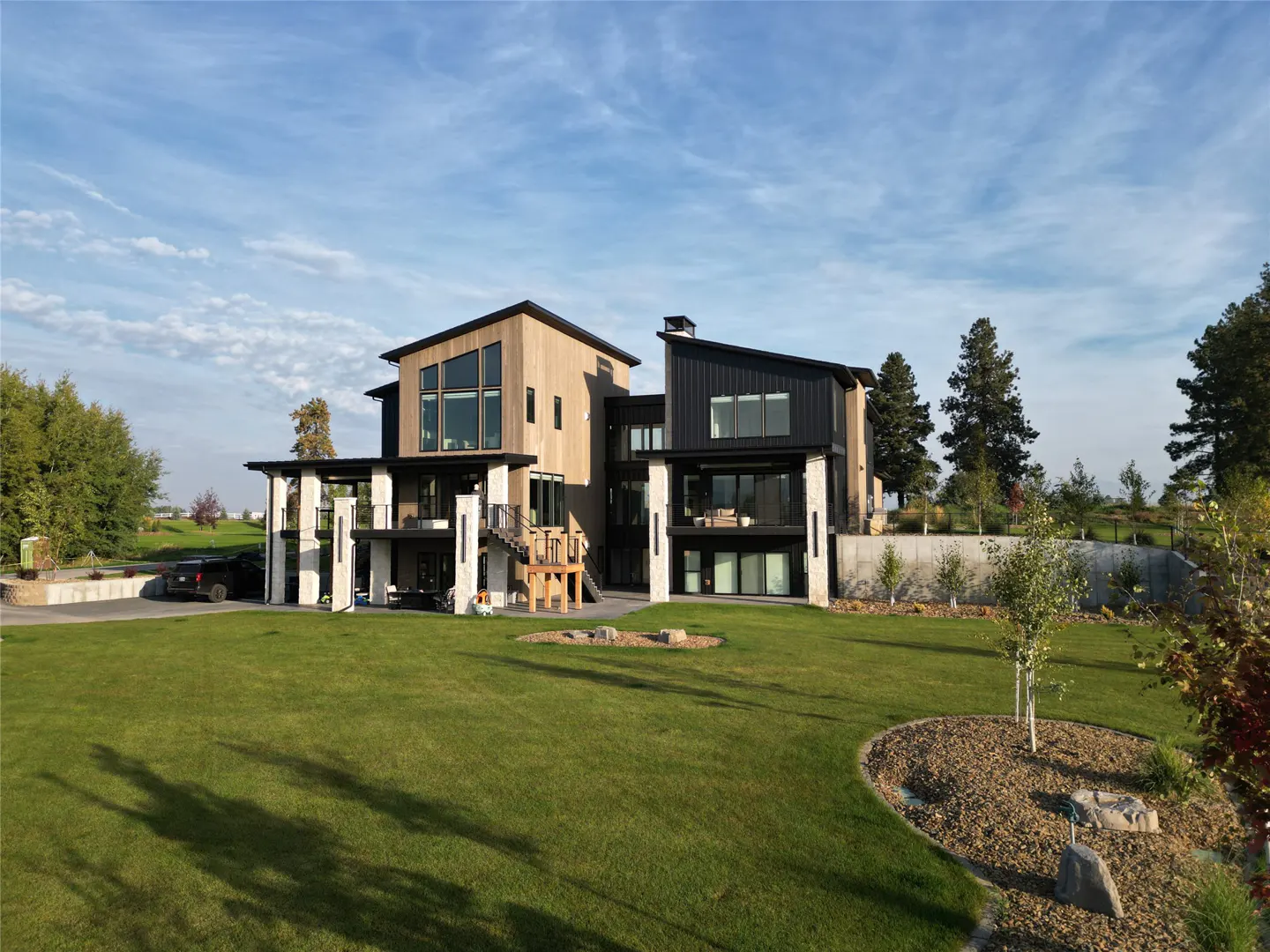 Modern two-story home with wood and black siding, large windows, and a green lawn under a blue sky.
