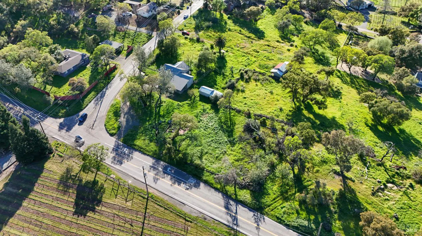 Aerial view of a rural landscape with houses, green fields, trees, and a road with cars.