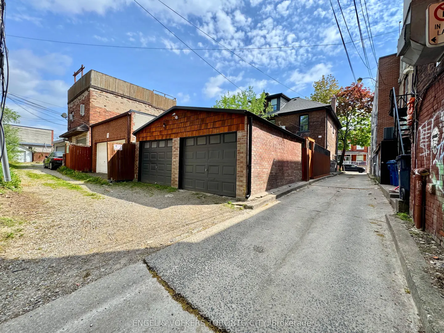 A narrow alleyway with brick buildings and garages under a blue sky.
