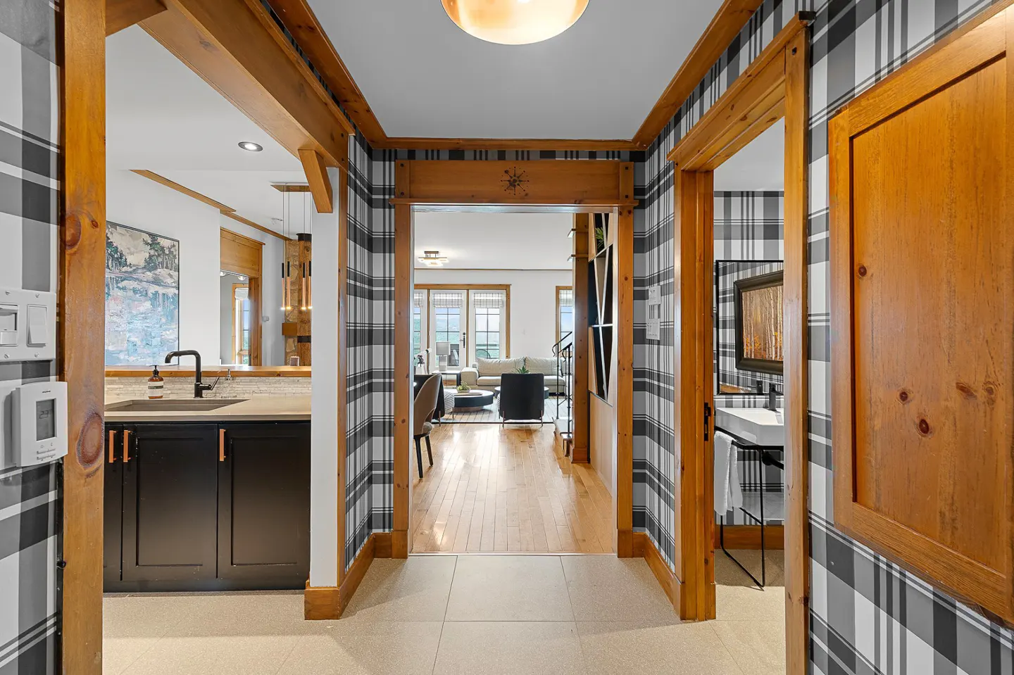 Hallway with black and white plaid wallpaper, wood trim, and tile floor. Living room and bathroom visible through doorways.