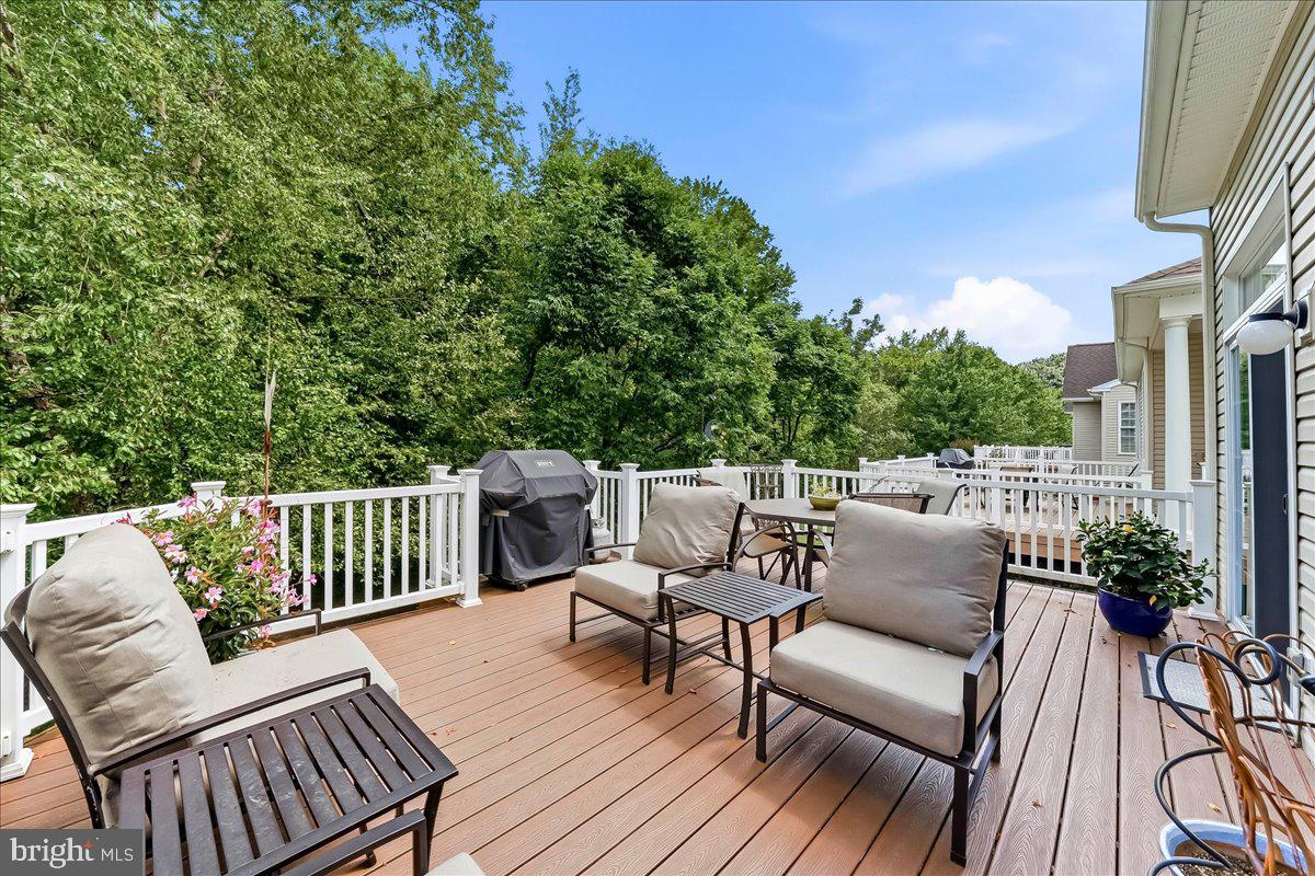 Spacious wooden deck with patio furniture, a grill, and white railings overlooking lush green trees under a blue sky. [AI-generated text]