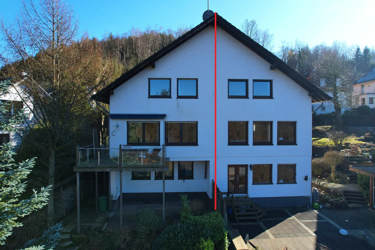 Two-story white house with a black roof, surrounded by trees and greenery. A satellite dish is on the roof.