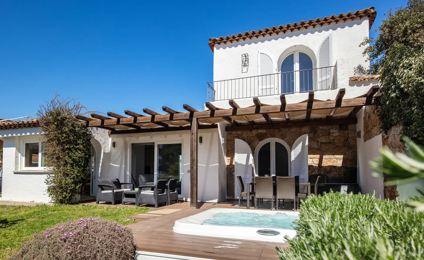Exterior of a white two-story house with a hot tub, patio furniture, and a wooden pergola.