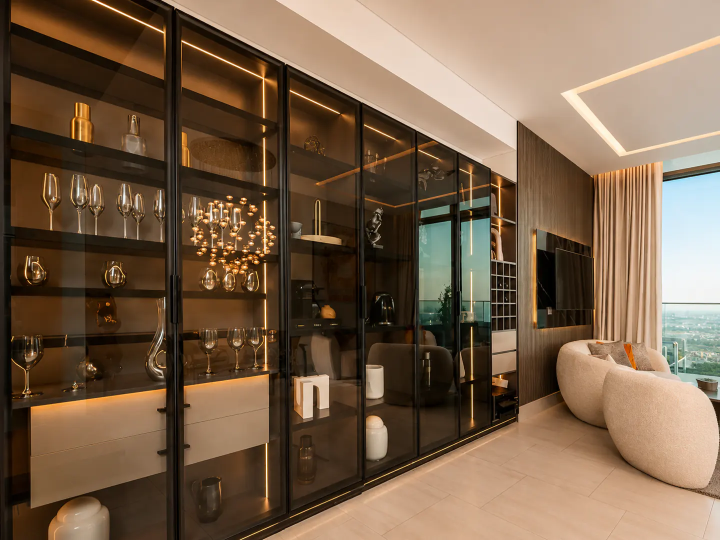 Modern living room with a large, illuminated glass-front display cabinet, cream-colored armchairs, and a city view.