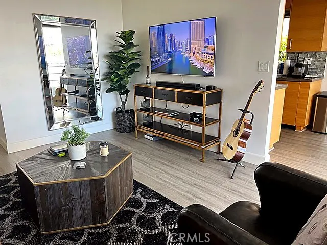Living room with a TV, a black and gold console table, a guitar, and a large mirror. A wooden coffee table sits on a patterned rug.