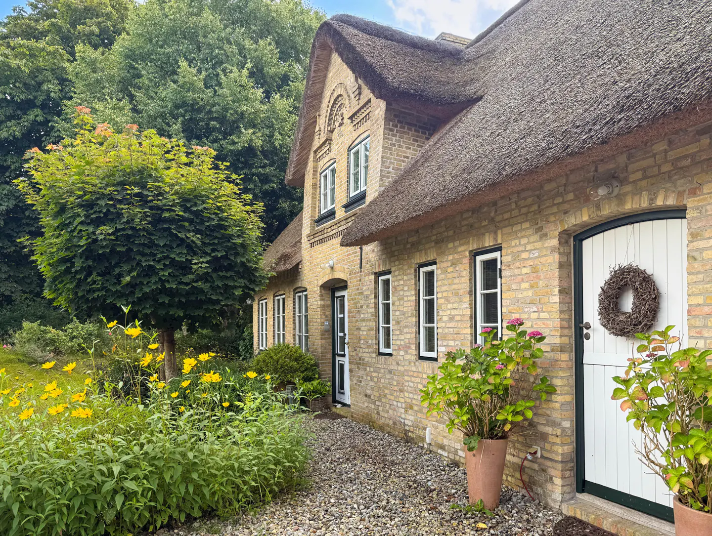 Exterior view of a tan brick house with a thatched roof, white trim, and a wreath on the front door.