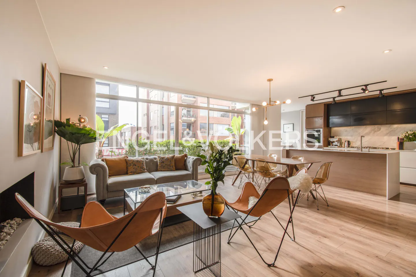 Open-concept living space with hardwood floors, a gray sofa, orange butterfly chairs, and a modern kitchen with an island.