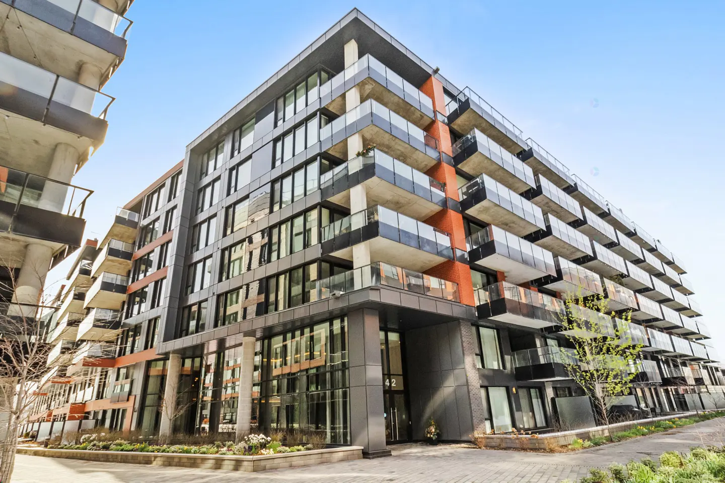 Modern condo building with glass balconies and a brick and gray facade under a blue sky.