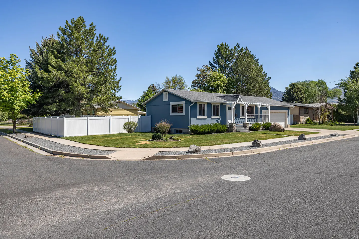 Blue single-story house with white trim, a pergola, and a white fence on a corner lot.