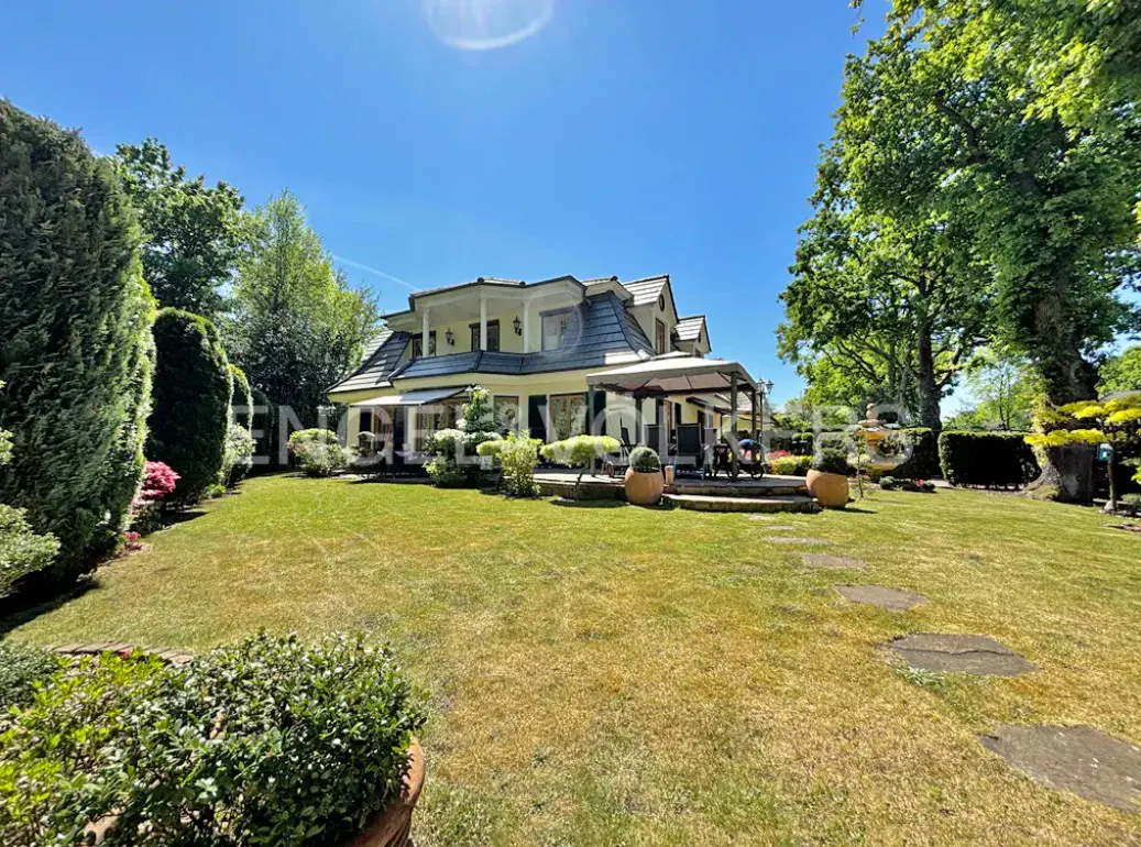 Two-story house with a gray roof and yellow siding, surrounded by a green lawn and trees under a blue sky.