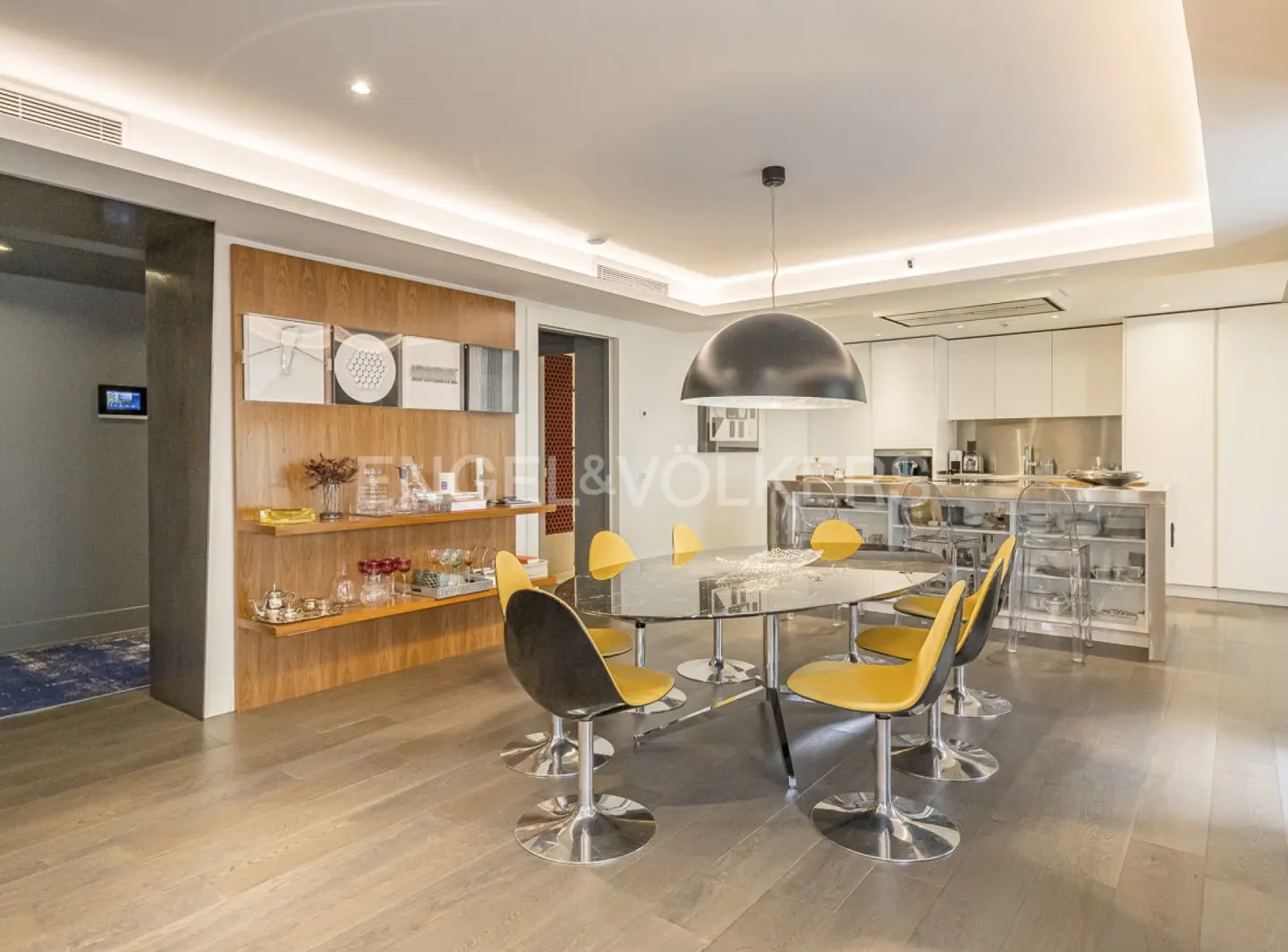 Open-concept dining area with a glass table, yellow chairs, and a modern kitchen in the background.