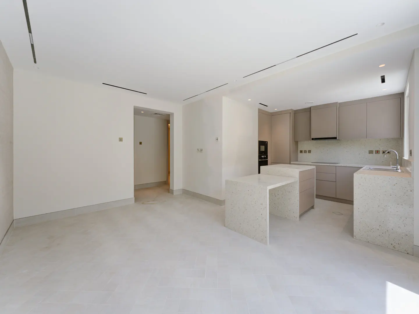 Bright, open-concept kitchen and living area with white walls and floors. Kitchen features gray cabinets and speckled white countertops.