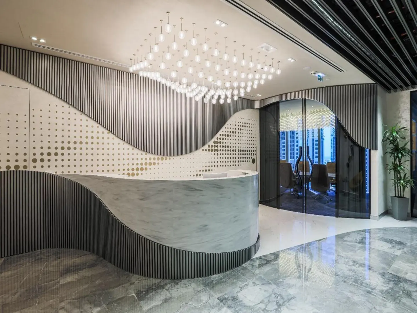 Modern office lobby with a marble reception desk, striped wall accents, and a decorative light fixture. A glass-walled conference room is visible.