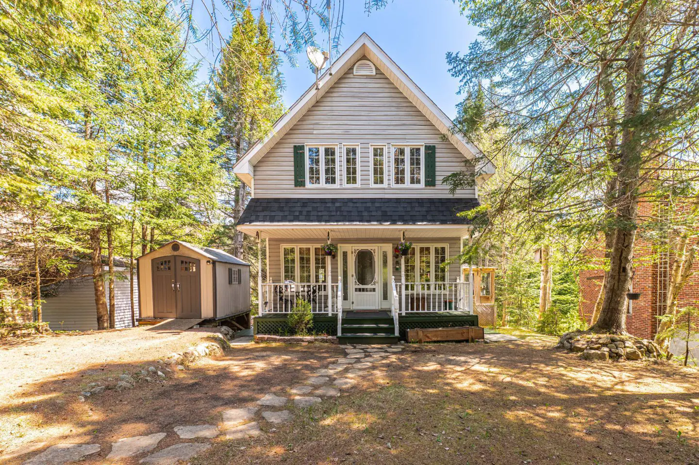 Two-story gray house with white trim and green shutters, surrounded by trees. A shed is to the left of the house.