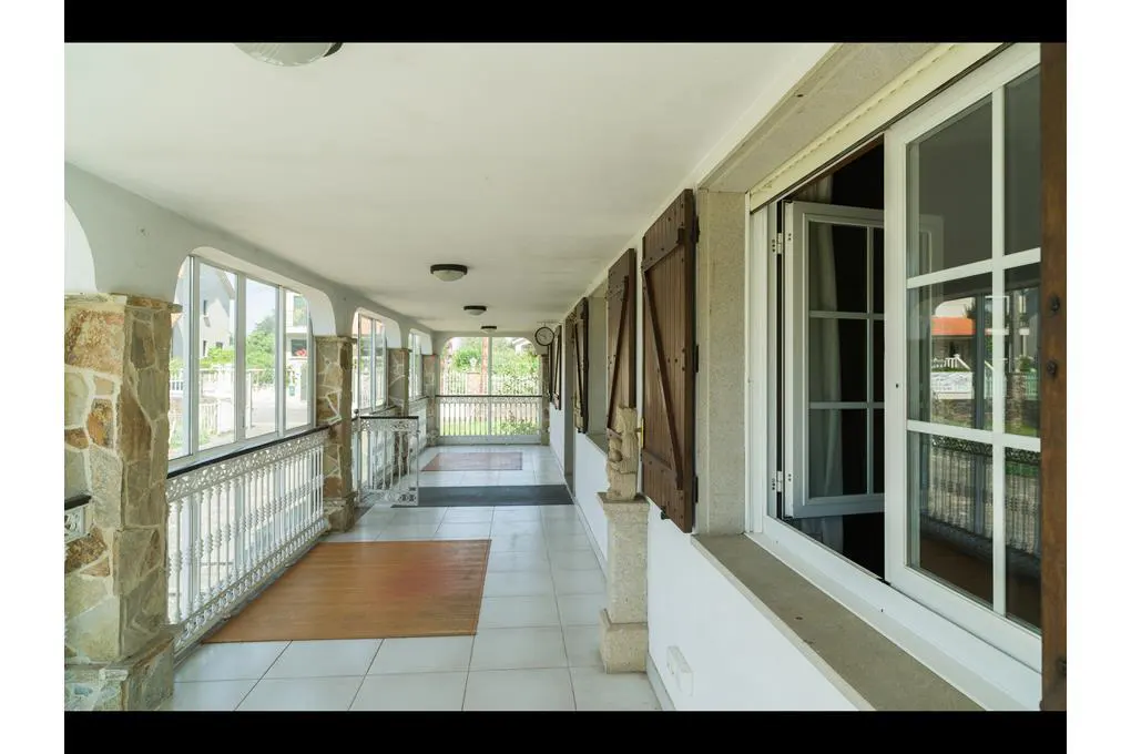 Covered porch with white tile floor, stone columns, and white railings. Windows with brown shutters line the right side.