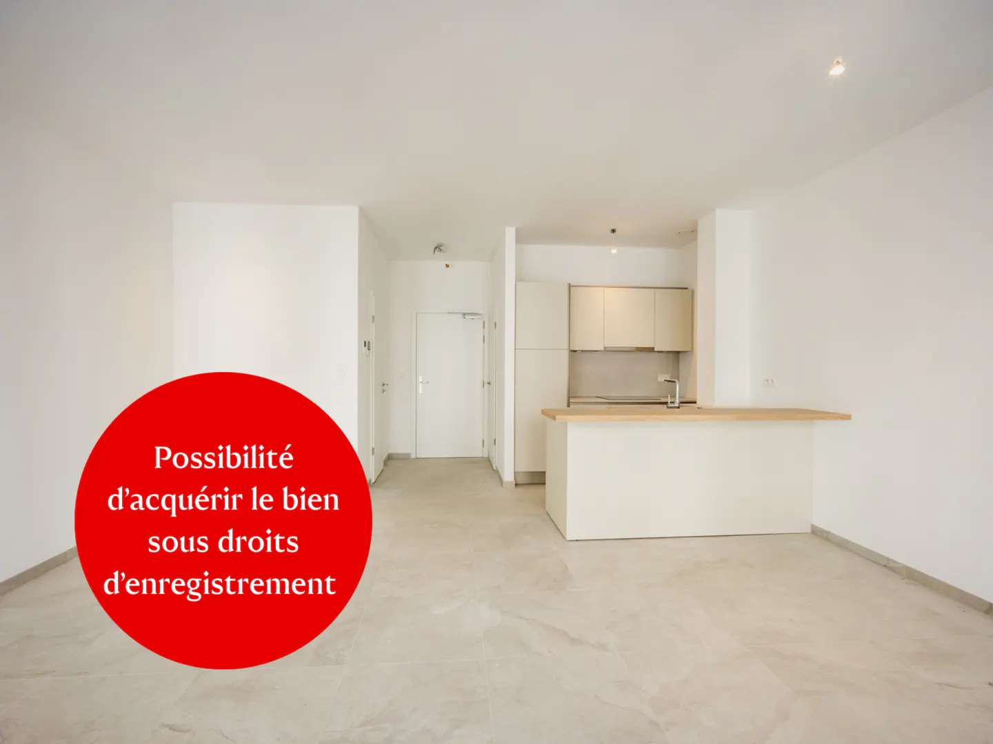Bright, empty apartment with white walls, light gray tile floor, and a small kitchen area with a breakfast bar. A red circle with white text is in the foreground.