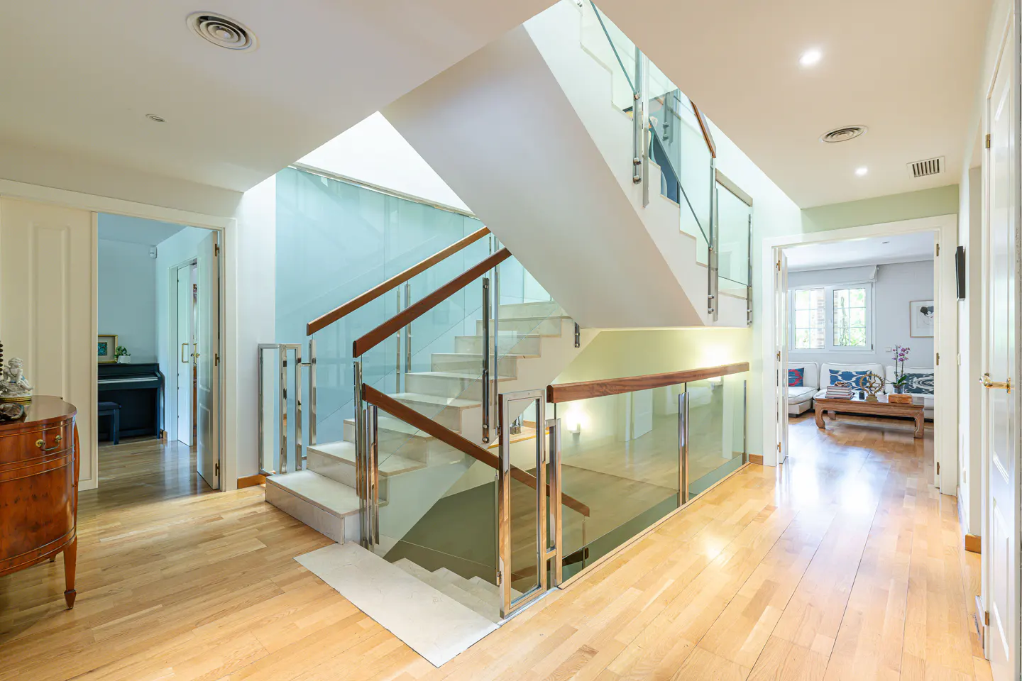 Modern staircase with glass railings and wooden handrails in a bright home with hardwood floors and open doorways.