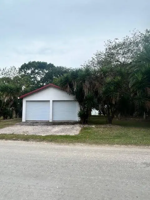 A white two-car garage with a red roof, surrounded by trees and green grass.