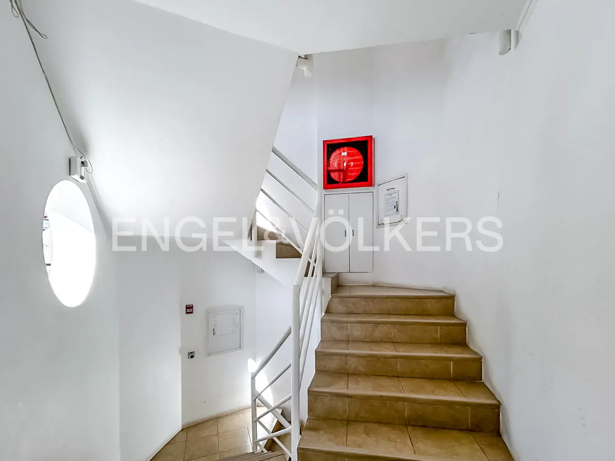 Interior view of a white stairwell with tan tile steps and white railings. A red fire hose cabinet is mounted on the wall.