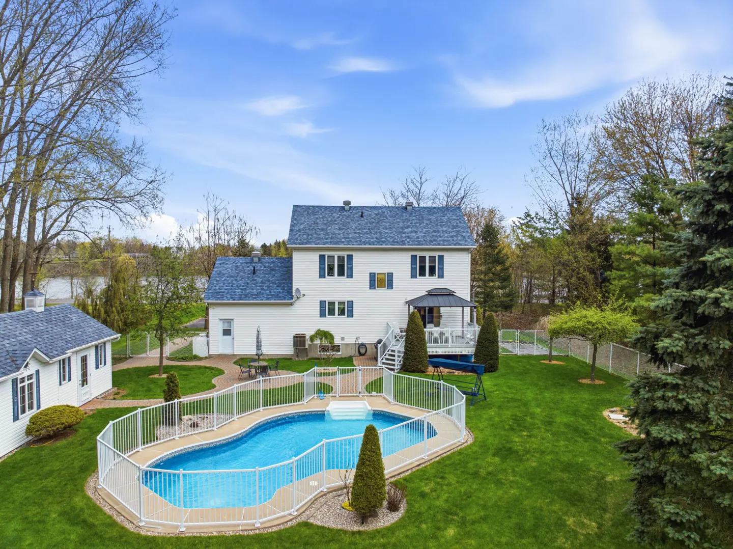 Aerial view of a white two-story house with a blue roof, a fenced-in blue swimming pool, and a green lawn.