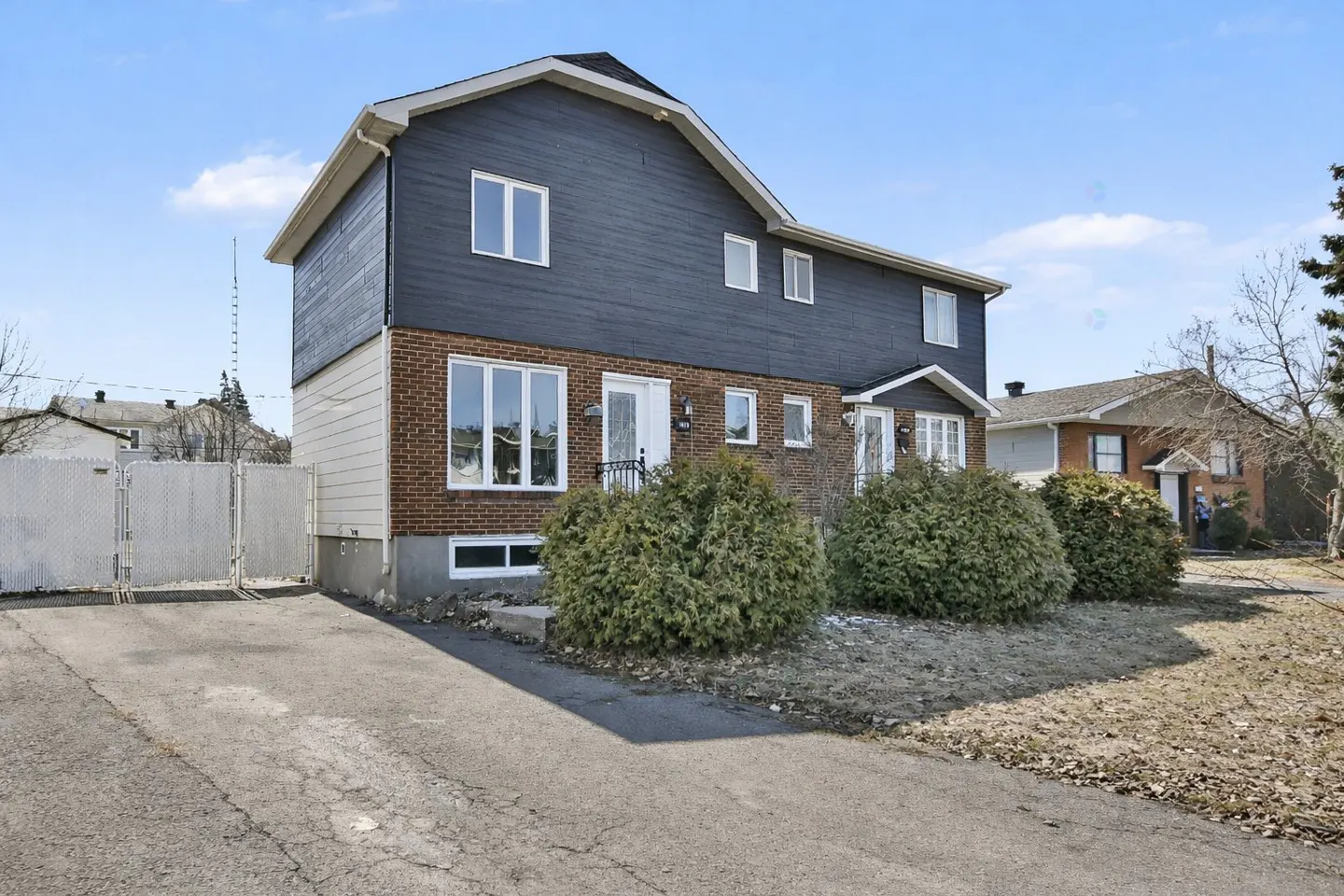 Two-story house with blue siding and brick facade, white trim, and a paved driveway on a sunny day.